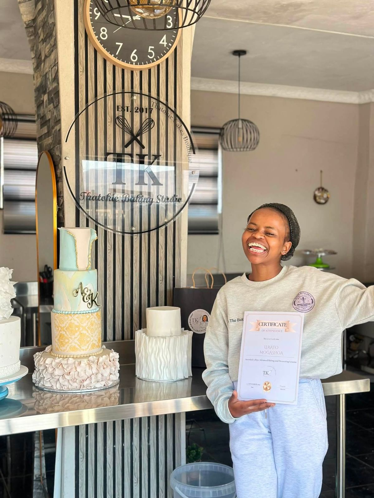 Lerato laughing and holding her certificate of attendance for advanced baking and decorating lessons