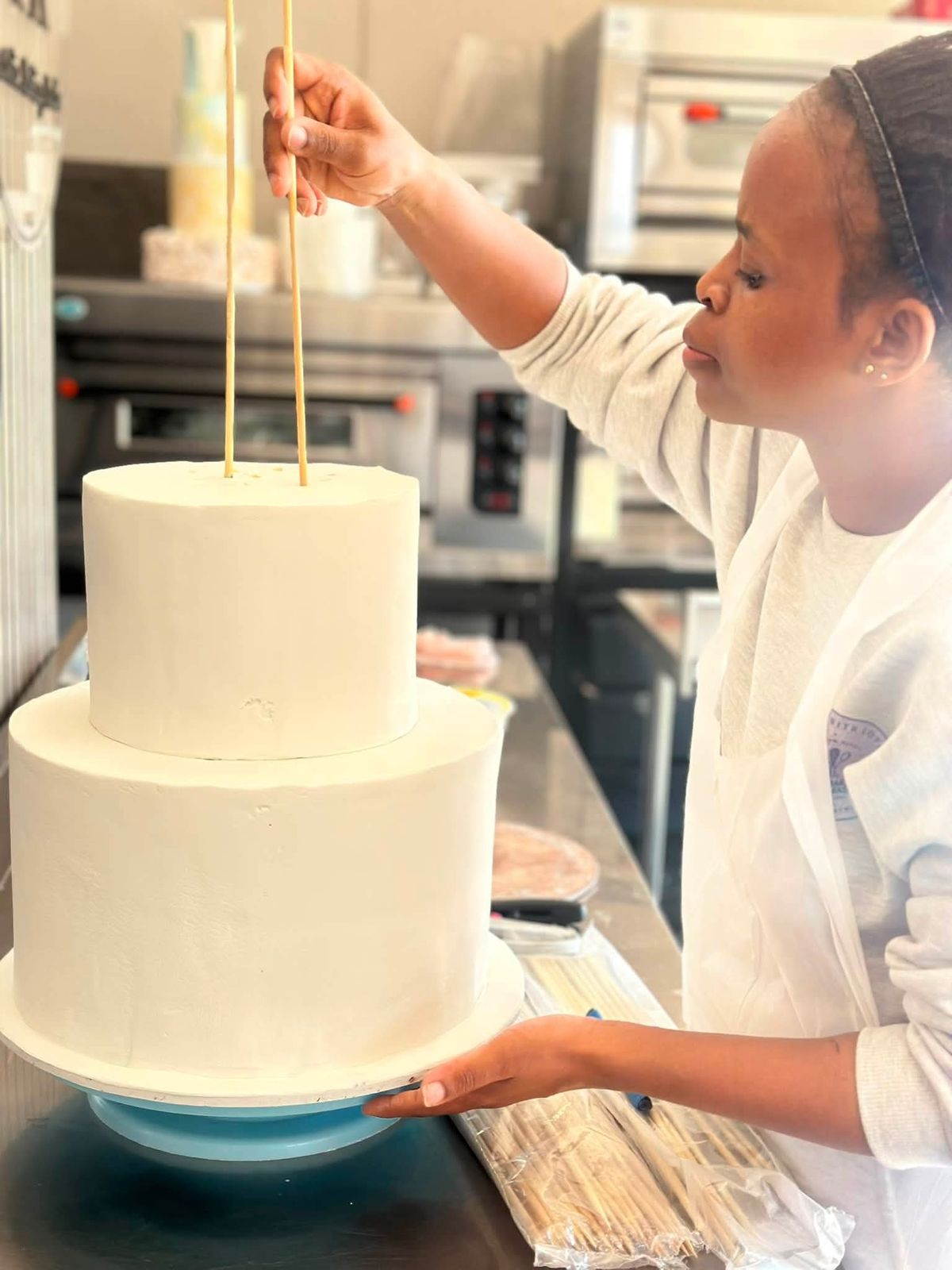 Lerato placing support dowels in a two-tier cake