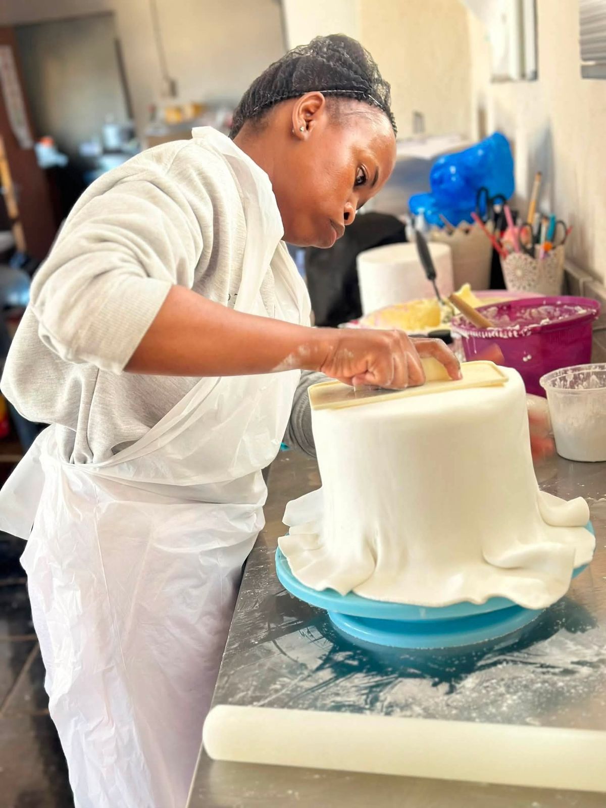 Lerato smoothing white fondant over a tall cake