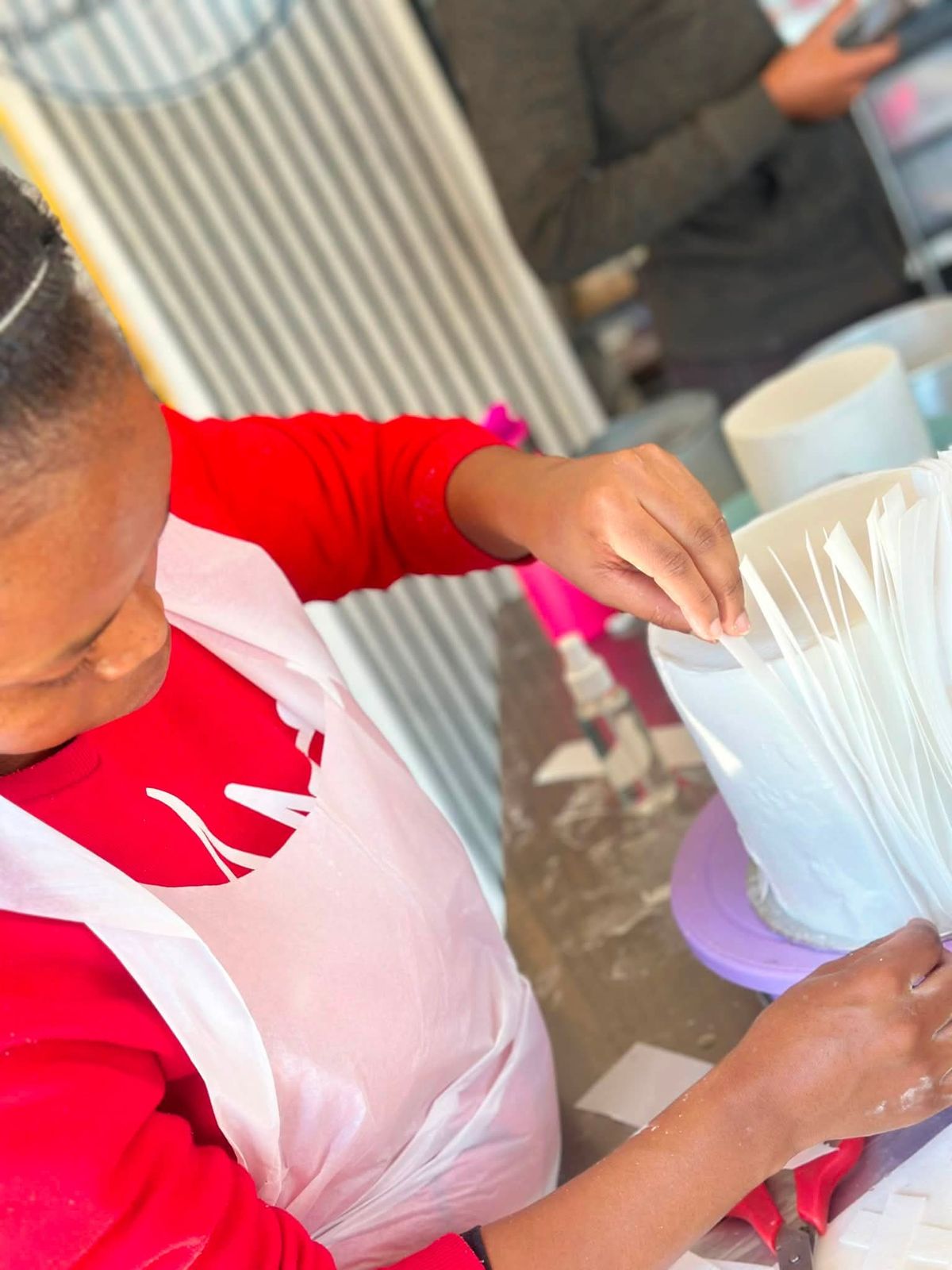 Hands arranging wafer-paper ruffles around a white cake