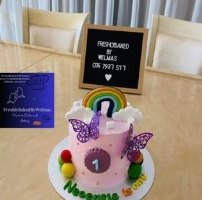 A pink first-birthday cake with a rainbow, butterflies and a number one