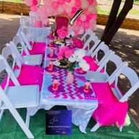 A hot-pink kiddies table with white chairs and a balloon arch on the lawn